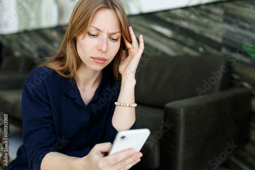 Young woman sad,reading bad news email, break up message from ex-boyfriend on smartphone sitting lonely on couch in living room. Depressed unhappy female desperate of heartbreak sms on mobile phone