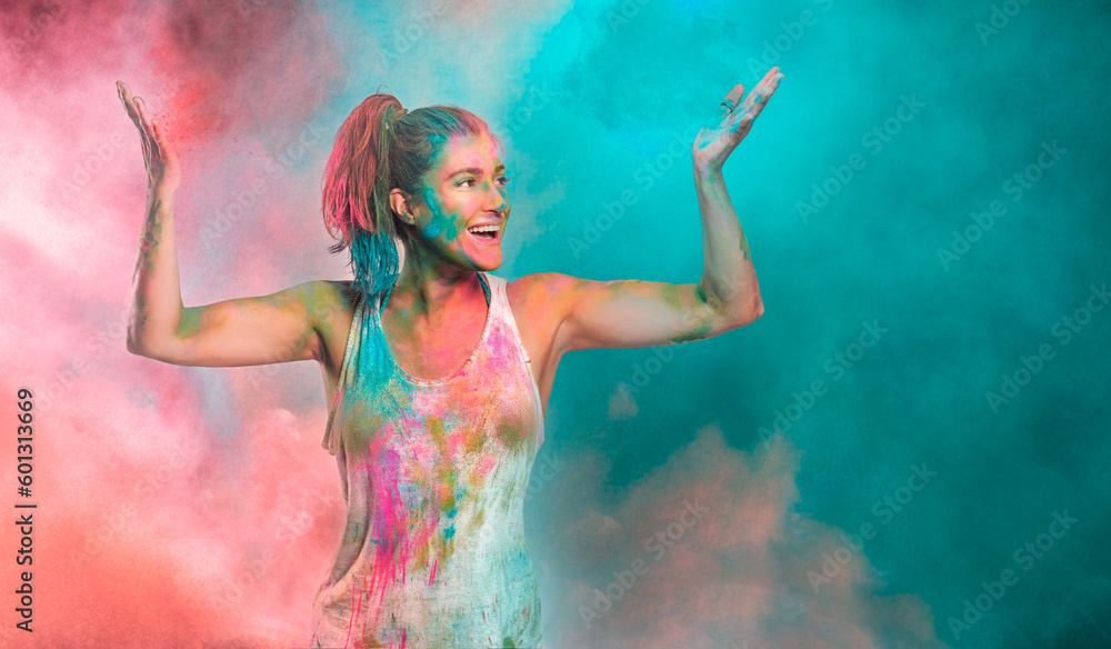 Carefree cheerful woman covered in rainbow colored powder celebrating the festival of colors. Young woman having fun with colorful holi powder