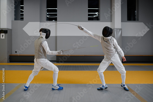 Athletes in uniforms and protective helmet mask fighting duel with rapiers