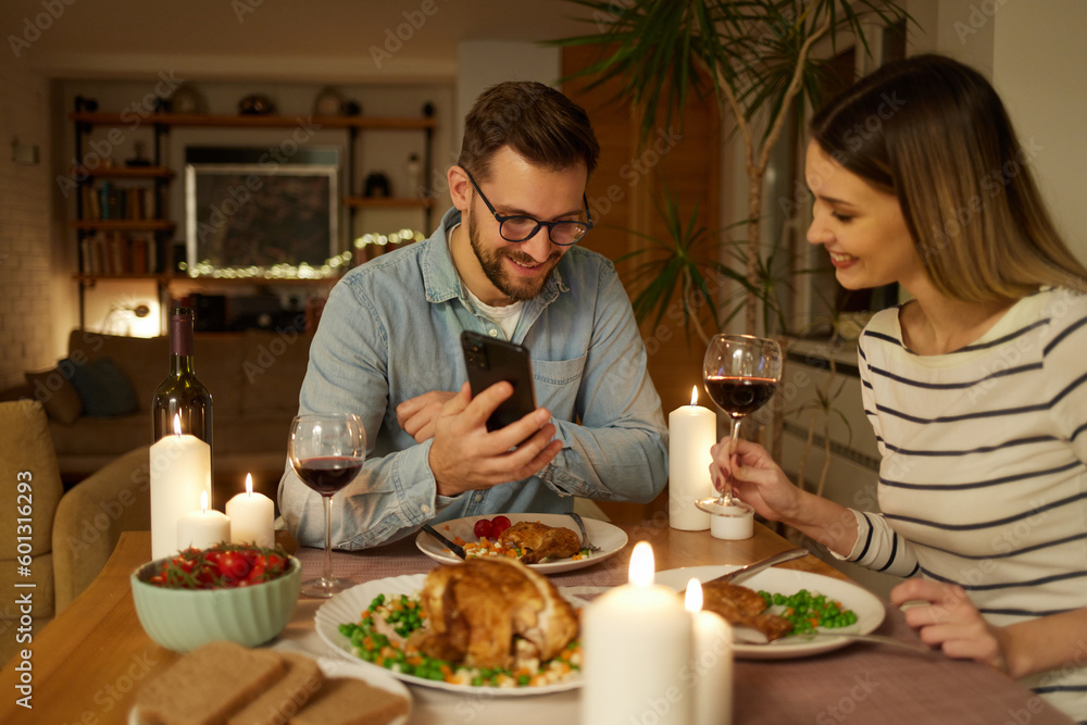 Happy couple enjoying food and wine while surfing the net on smart phone at home Happy couple enjoying food and wine while surfing the net on smart phone at home