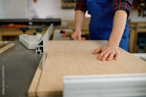 Closeup of carpenter cutting wooden board on circular saw workbench