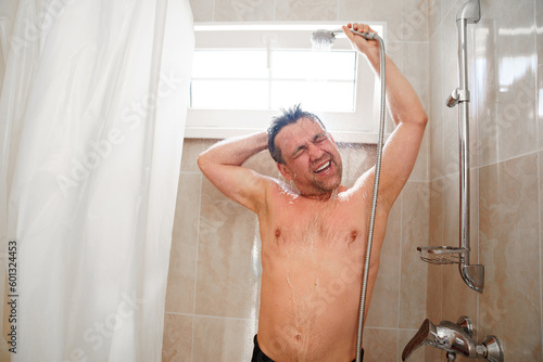 an ordinary man takes a shower and washes his hair in a small bathroom with a shower head on the wall, a curtain and a window for ventilation. Economical and simple interior for a house or hotel.