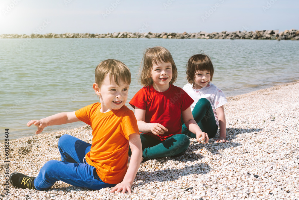 Children sit on a beach made of shells and squint from the sun look to the side. Copy space. International Children's Day concept Children sit on a beach made of shells and squint from the sun look to the side. Copy space. International Children's Day concept