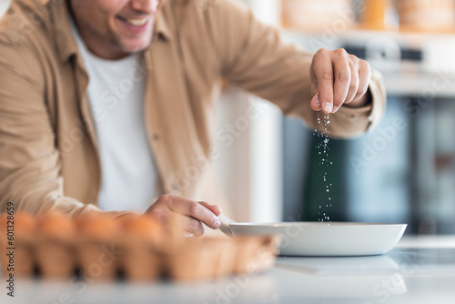 Photos A smiling man makes scrambled eggs and salts them while they are in a pan