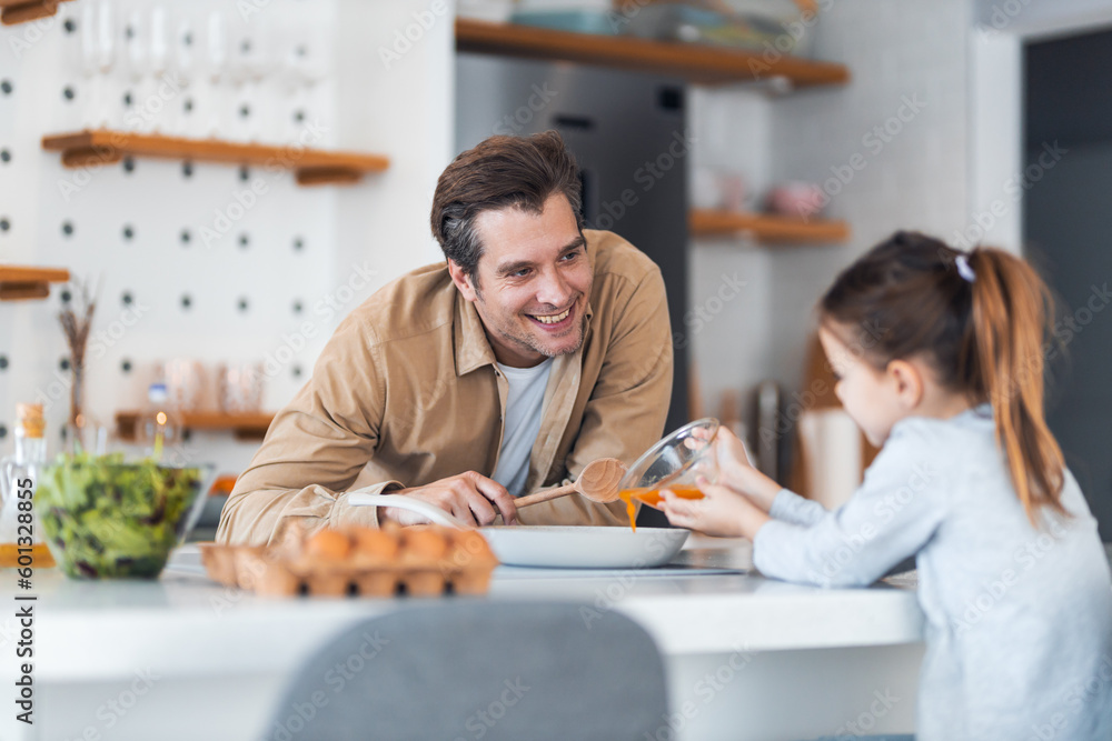 A father looking at how her daughter pours beaten yolks into the pan in the kitchen. A father looking at how her daughter pours beaten yolks into the pan in the kitchen.