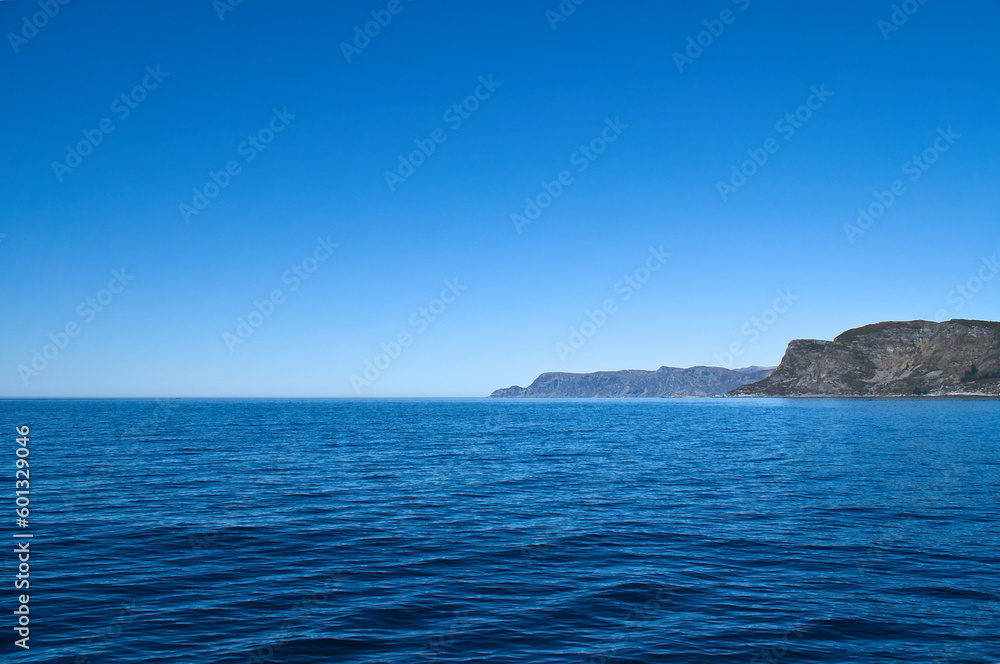 View from the sea to the West Cape in Norway in sunshine. Waves and rocks