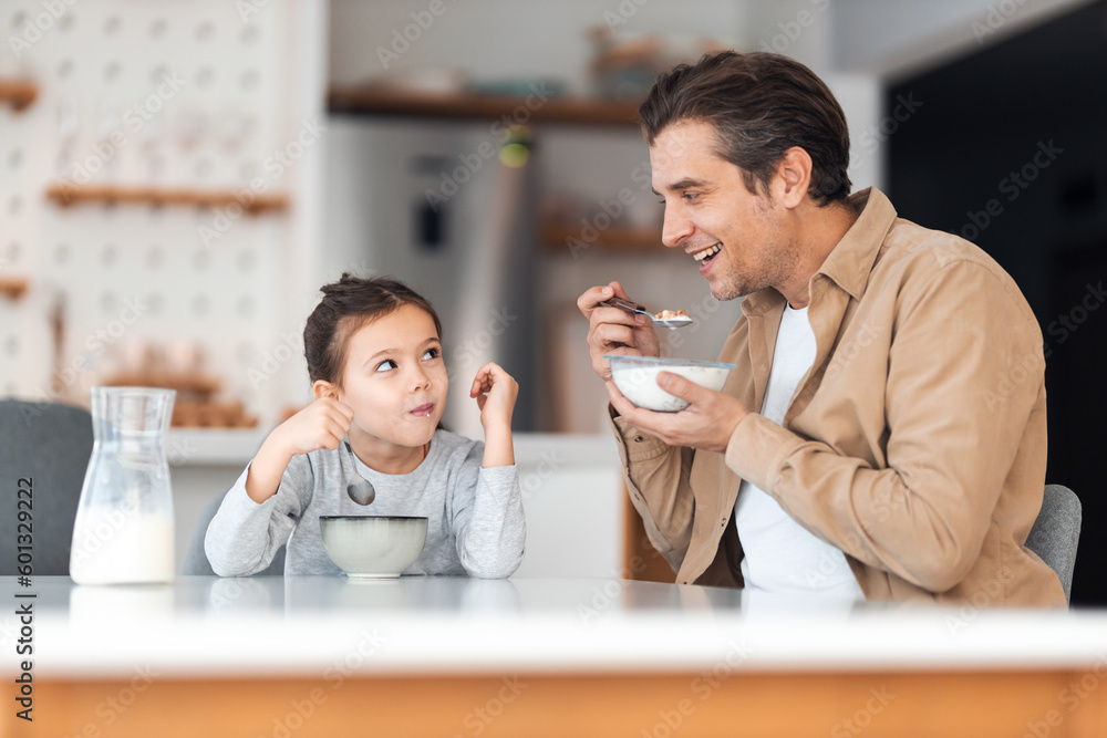 A smiling father having cereal with milk for breakfast with his cute daughter.