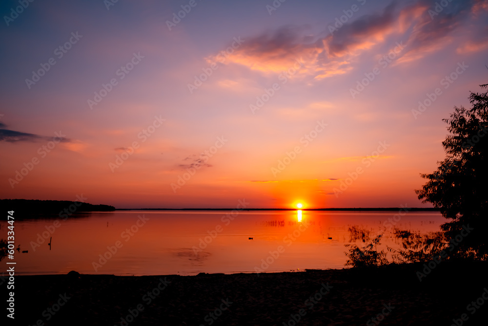 Beautiful sunset above the lake with blue sky and rare fluffy pink clouds. Sun path. Seascape. Calm water. Natural background. Nature landscape. Summertime travelling. Warm evening concept. No people