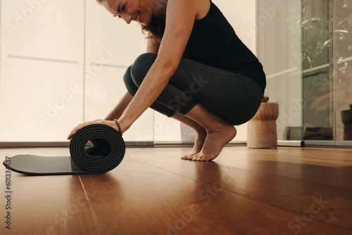 Obraz Smiling senior woman folding up a yoga mat at home