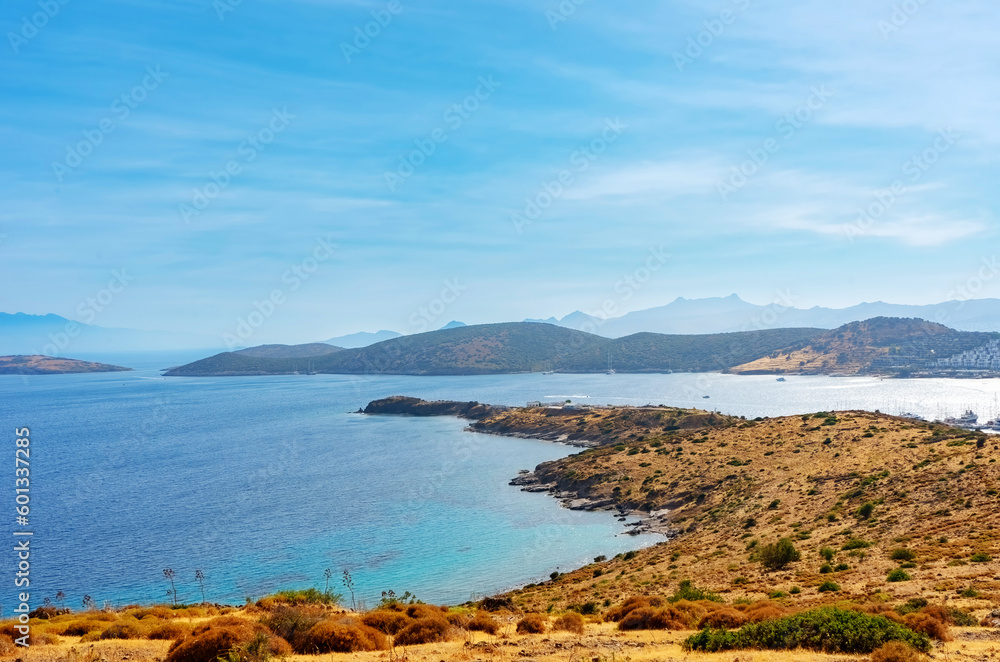 Peninsula with dried yellow grass in the blue sea with mountains in the background. Summer seascape, panorama, view of the bay. Travel, tourism, nature