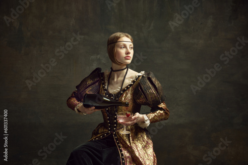 Portrait of young girl, princess in vintage dress pouring champagne into glass against dark green background. Party, celebration. Concept of history, renaissance art remake, comparison of eras