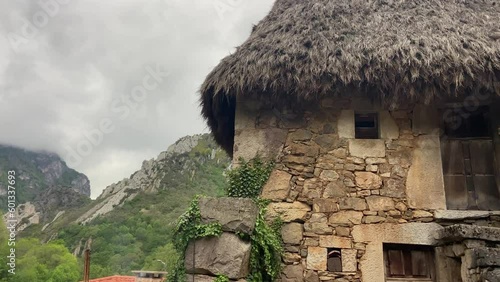 Close-up of an old stone hut with thatched roof in the middle of a green valley on a cloudy day photo