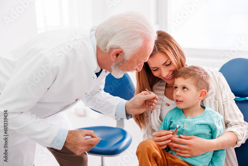 Dentist checking up little boy sitting in mother s lap