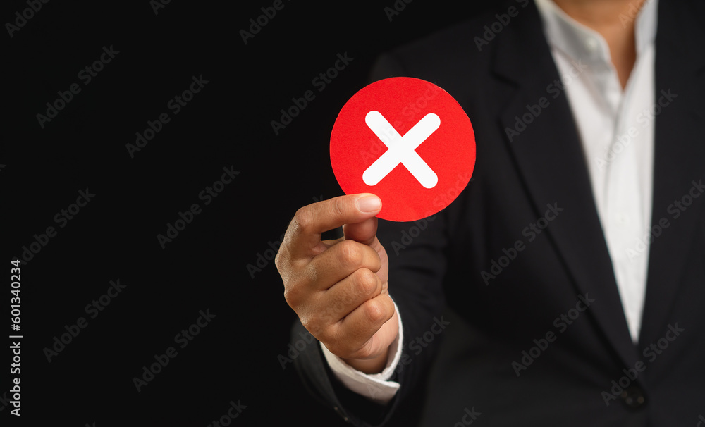 Businessman in a suit holding a cross symbol while standing on a black backgroun Businessman in a suit holding a cross symbol while standing on a black backgroun