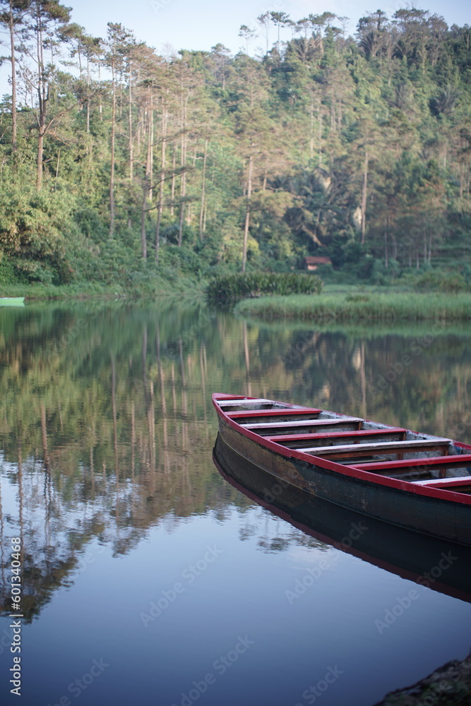 A wooden boat floating on a calm lake surrounded by trees at dawn, creating a peaceful and serene atmosphere perfect for a relaxing morning ride