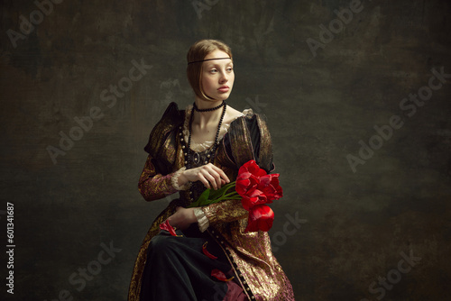 Portrait of beautiful young girl, royal person, queen in elegant vintage dress posing with flowers, tulips against dark green background. Concept of history, renaissance art remake, comparison of eras