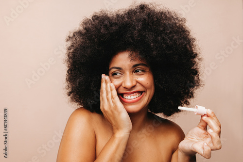 Young woman with Afro hair applying beauty oil on her face