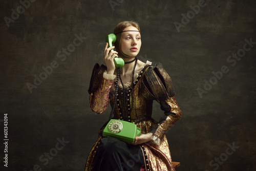Quadro su tela Portrait of young girl in vintage dress, royal person talking on retro phone against dark green background