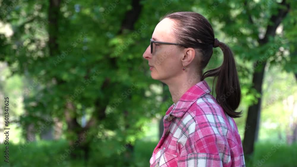 Woman in glasses and pink shirt walking in grove deciduous trees. Middle adult with hair horsetail looking on green foliage and dream. Leisure person of 39-49 years looking on spring landscape. Hiking Woman in glasses and pink shirt walking in grove deciduous trees. Middle adult with hair horsetail looking on green foliage and dream. Leisure person of 39-49 years looking on spring landscape. Hiking