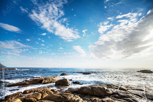 Rock, ocean and nature with waves at beach for environment, landscape and blue sky. Calm, summer and seascape with sunrise on horizon at coastline for tropical, clouds and water surface