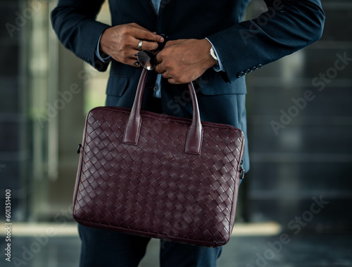 Corporate businessman walking and holding a maroon leather patterned bag