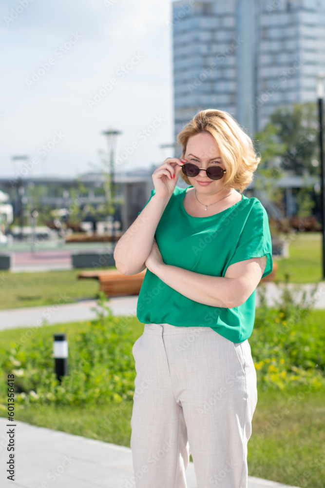 A beautiful stylish slender woman in a green blouse touches sunglasses with her hands