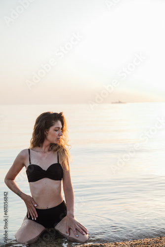 Fototapeta Naklejka Na Ścianę i Meble -  woman in black swimsuit sitting in the water in the sea relaxing on the beach