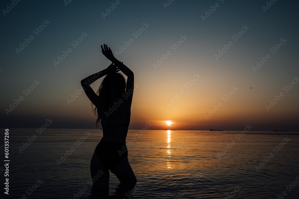 silhouette of a woman in a swimsuit on the beach at sunset by the sea walk rest