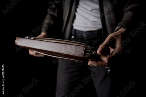Creative shot of man opening a brown leather laptop bag in studio black background