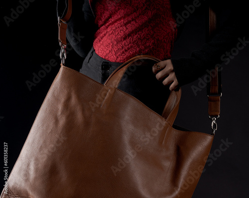Woman casually holding a brown leather big bag in studio black background