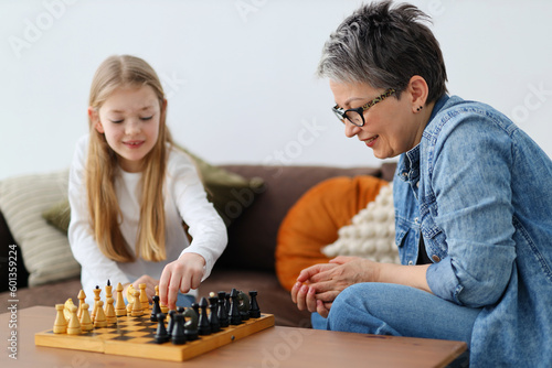 Happy and innocent little granddaughter plays chess with her grandmother.