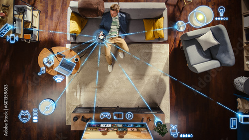 Fotografija Top View Of Caucasian Man In the Loft Apartment Sitting Down on The Couch and Connecting Smartphone to Convenient Smart Home System
