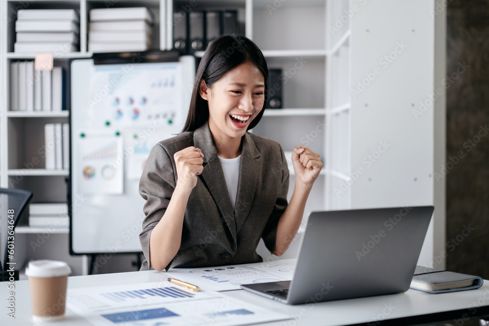 Accounting business concept, Accountant woman reads good news on laptop with excited and raising fist to celebrate achievement while working about investment with business planning finance Accounting business concept, Accountant woman reads good news on laptop with excited and raising fist to celebrate achievement while working about investment with business planning finance
