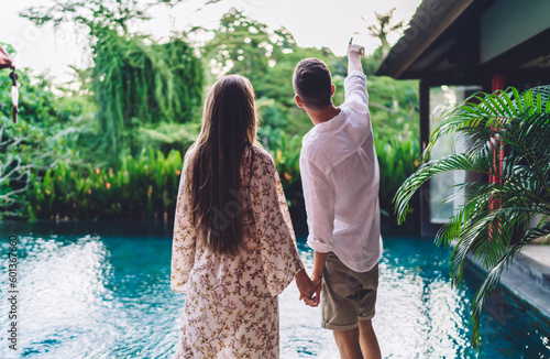 Back view of Caucaisan couple in love discussing summer nature at villa terrace with pool during honeymoon in Indonesia, young husband and wife in casual clothes spending travel vacations at Bali #601367660