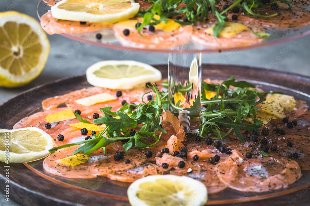 Salmon carpaccio with lemon and rocket on a cake stand, italian starter, antipasti, gray background, close up. Salmon carpaccio with lemon and rocket on a cake stand, italian starter, antipasti, gray background, close up.
