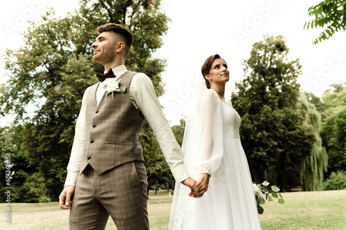modern newlyweds in rustic style. wedding couple holding hands standing with their backs to each other. wedding outside in summer. attractive wedding couple