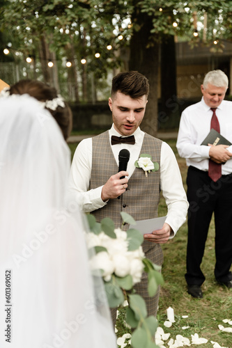 A handsome groom makes an oath to the bride at the wedding ceremony. wedding ceremony outside. nesta with the groom on the background of the wedding arch
