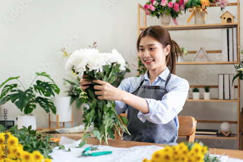 Female florist in apron holding white chrysanthemum to creating