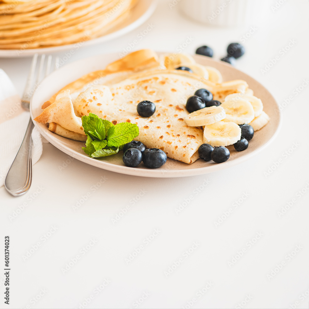 French crepes with banana and blueberries on white table. Copy space