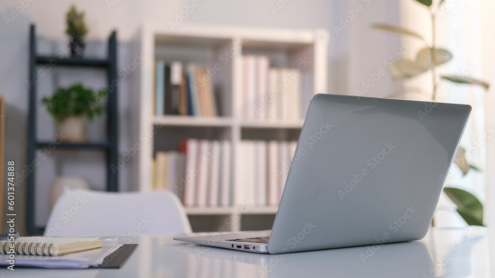 Comfortable office desk with laptop computer and notepad on white table.