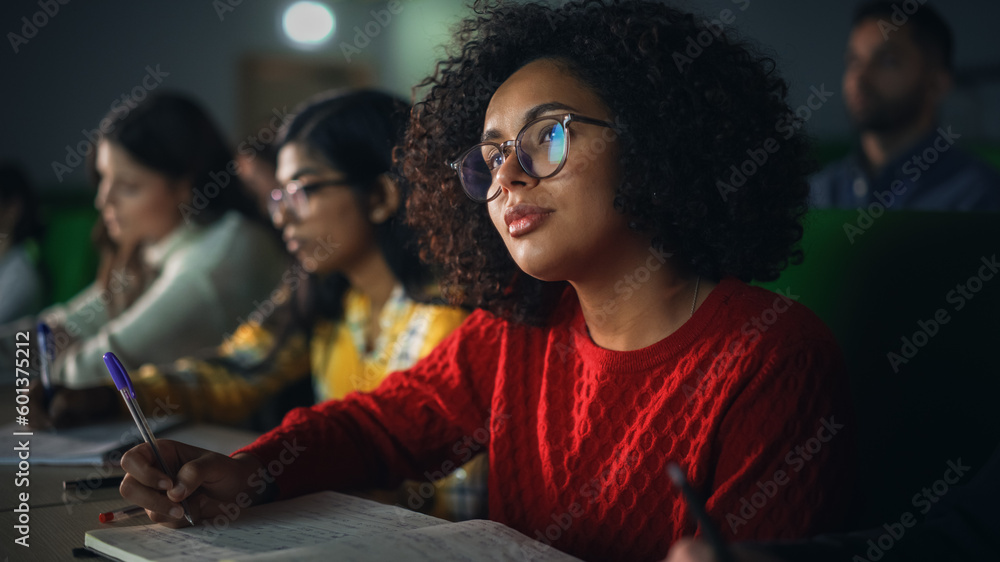 Fototapeta premium Talented Smart Multiethnic Hispanic Female Student Studying in College with Diverse Colleagues. Black Young Woman Writing Down a Summary from the Lecture in Her Notebook
