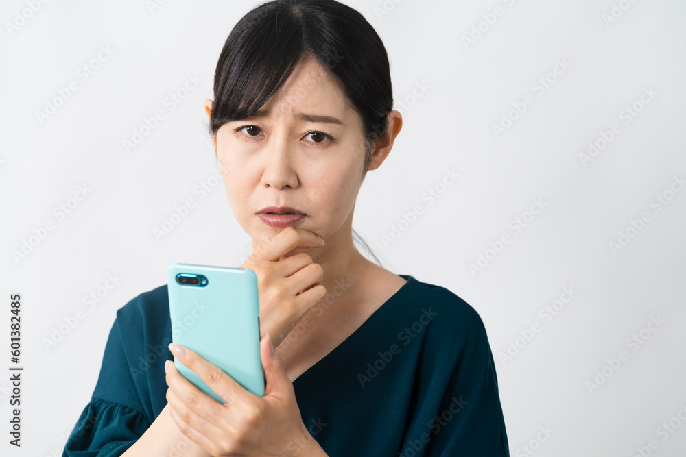 スマートフォンを持ちながらネガティブな表情をする若い女性 スマートフォンを持ちながらネガティブな表情をする若い女性