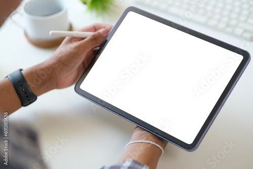 Close up view of man hand holding digital tablet over white working desk. Blank screen for