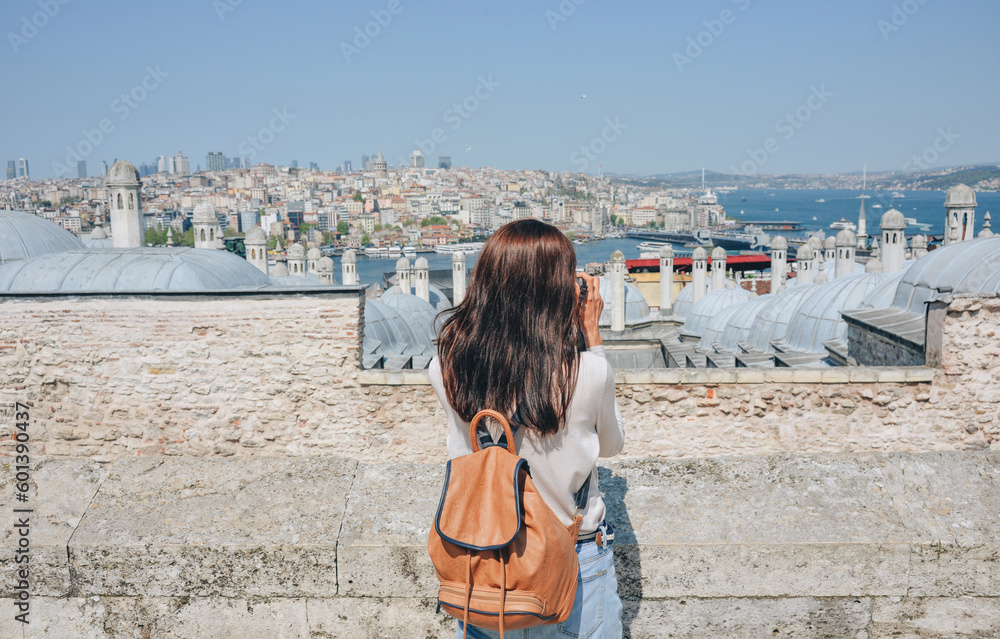 A young traveler with a backpack on her back looks at the landscape from the Suleymaniye Mosque on a sunny day in Istanbul.
