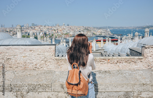 Photography A young traveler with a backpack on her back looks at the landscape from the Suleymaniye Mosque on a sunny day in Istanbul