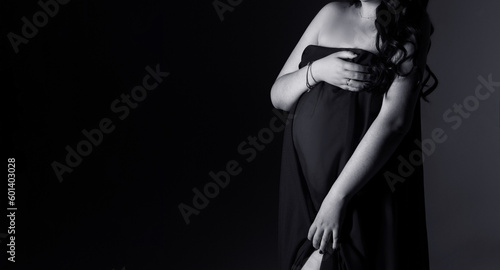 pregnancy woman in a black dress on a black background with copy space, studio pregnancy photo shoot