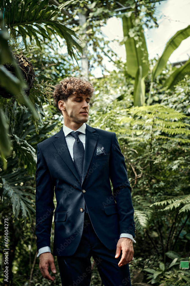 Handsome young man in blue suit posing in tropical garden Handsome young man in blue suit posing in tropical garden