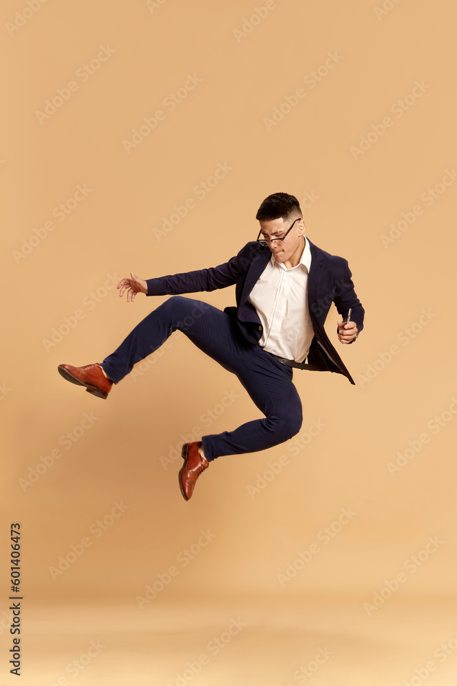 Portrait with happy man, guy wearing classical suit dancing after good job interview over beige color studio background. Hired