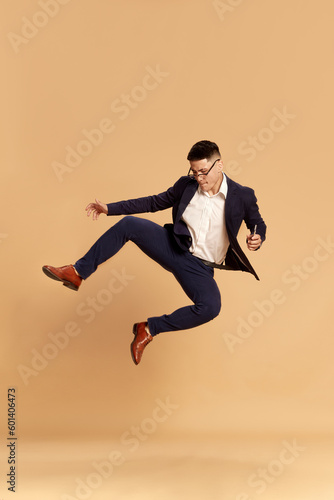 Portrait with happy man, guy wearing classical suit dancing after good job interview over beige color studio background. Hired