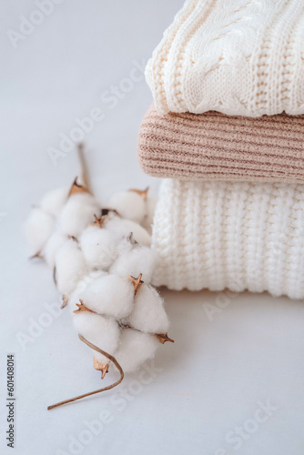 Stack of knitted sweaters with cotton flowers on white background.